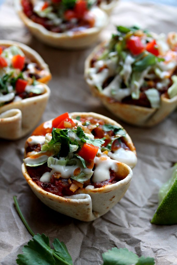 Close-up of crispy vegan taco cups filled with seasoned meat, vegan cheese, and fresh toppings.