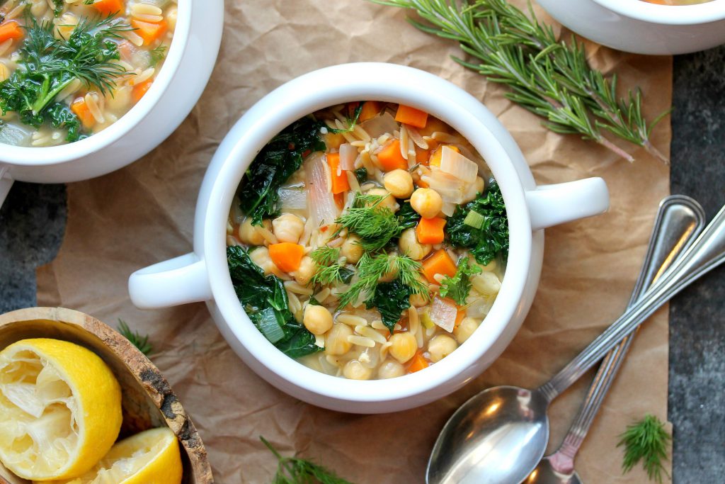 A bowl of Lemon Dill Chickpea Orzo Soup garnished with fresh dill and a lemon wedge, ready to be enjoyed.