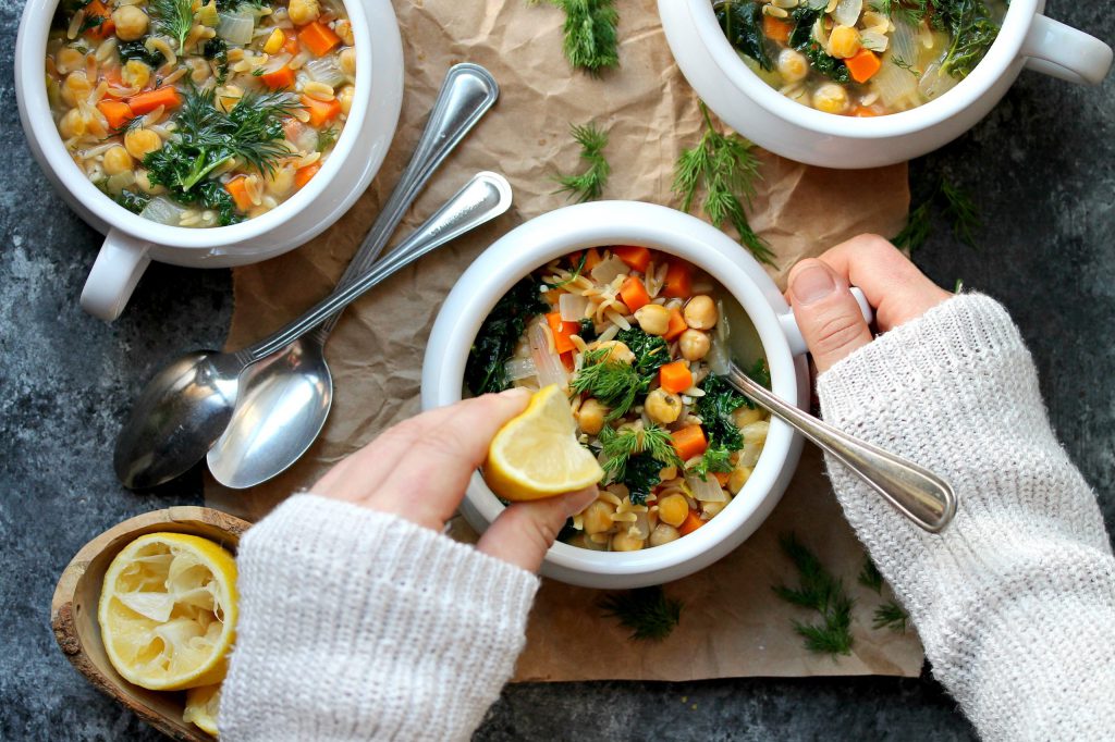 A bowl of Lemon Dill Chickpea Orzo Soup garnished with fresh dill and a lemon wedge, ready to be enjoyed.