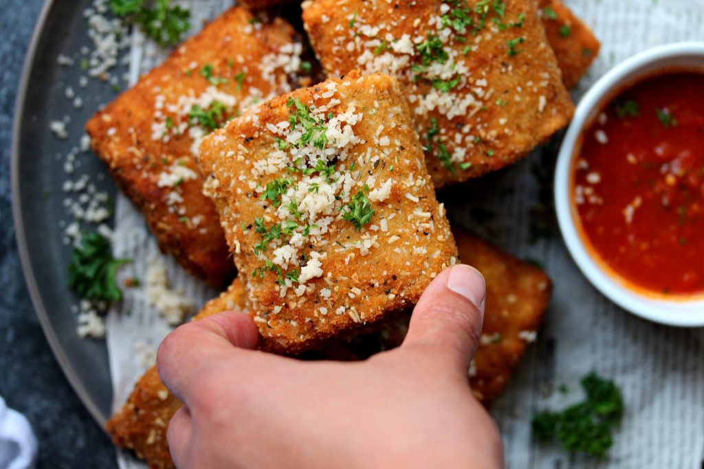 Crispy vegan lasagna fritta served with marinara sauce, garnished with fresh parsley and vegan parmesan.