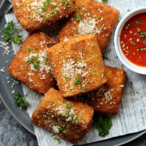 Crispy vegan lasagna fritta served with marinara sauce, garnished with fresh parsley and vegan parmesan.