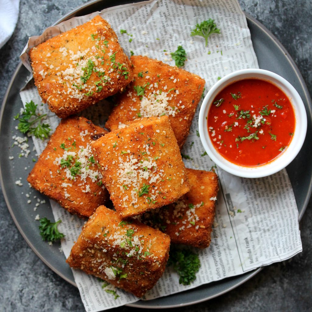 Crispy vegan lasagna fritta served with marinara sauce, garnished with fresh parsley and vegan parmesan.