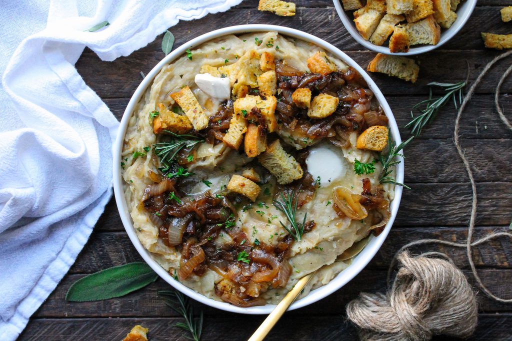 A bowl of creamy vegan French onion mashed potatoes topped with caramelized onions and crispy herby croutons.