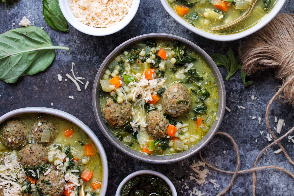 A close-up of a bowl of Pesto Italian Wedding Soup topped with vegan meatballs, kale, and julienned basil.