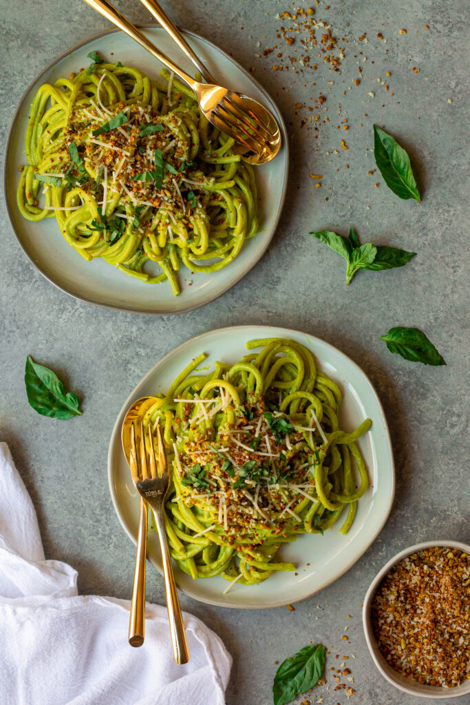 Creamy zucchini pasta served in a bowl, topped with vegan parmesan, fresh basil, and lemony pistachio breadcrumbs.