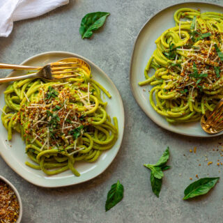 Creamy zucchini pasta served in a bowl, topped with vegan parmesan, fresh basil, and lemony pistachio breadcrumbs.