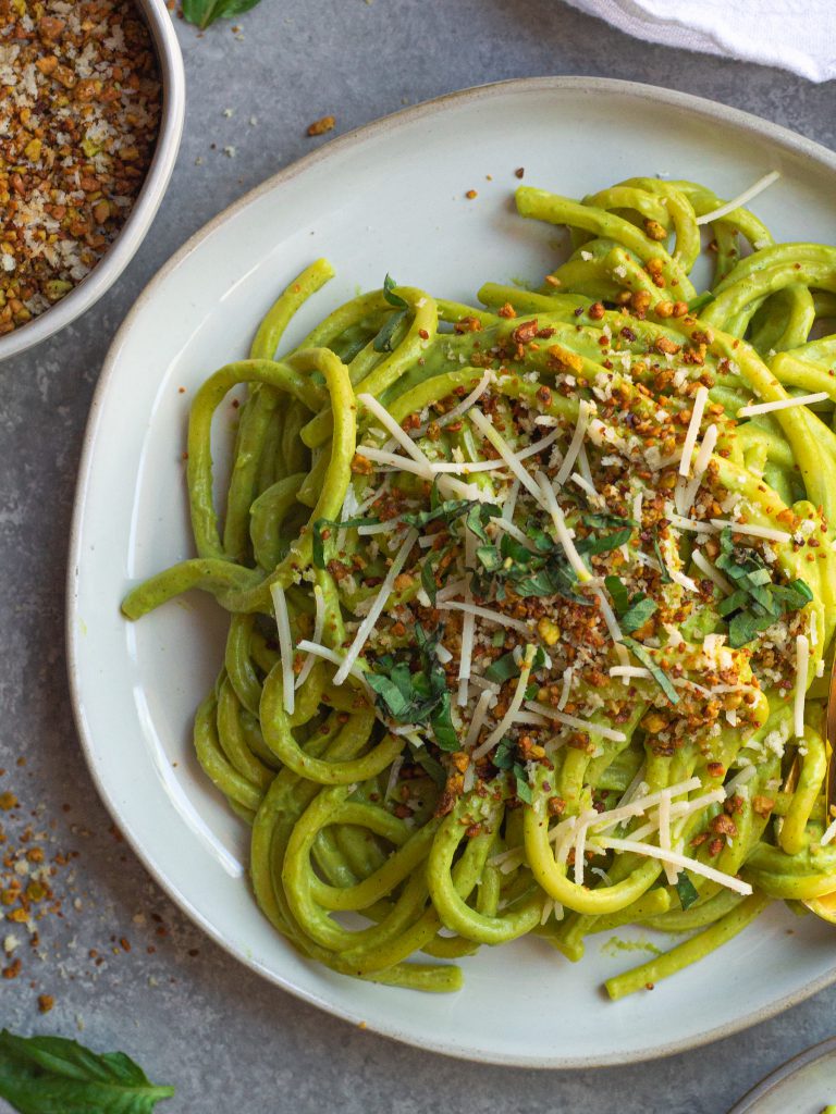 Creamy zucchini pasta served in a bowl, topped with vegan parmesan, fresh basil, and lemony pistachio breadcrumbs.