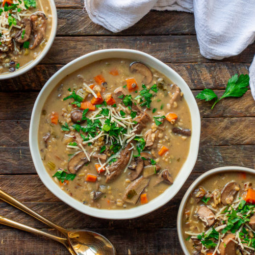 Bowl of creamy vegan wild rice and mushroom soup garnished with fresh parsley and vegan parmesan cheese.