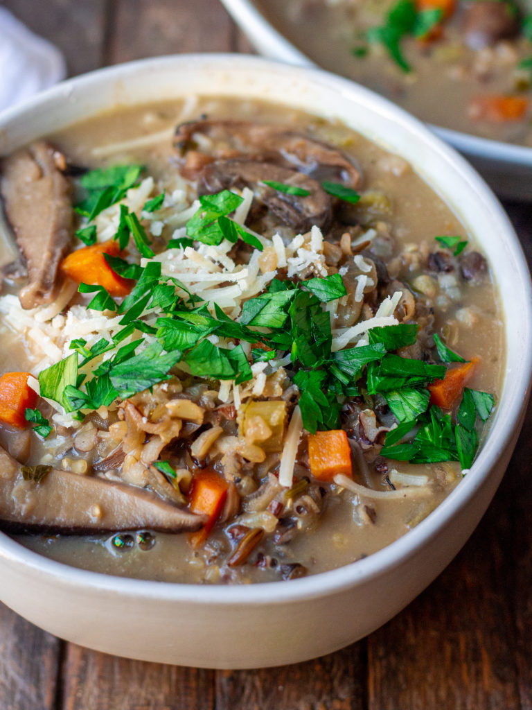 Bowl of creamy vegan wild rice and mushroom soup garnished with fresh parsley and vegan parmesan cheese.