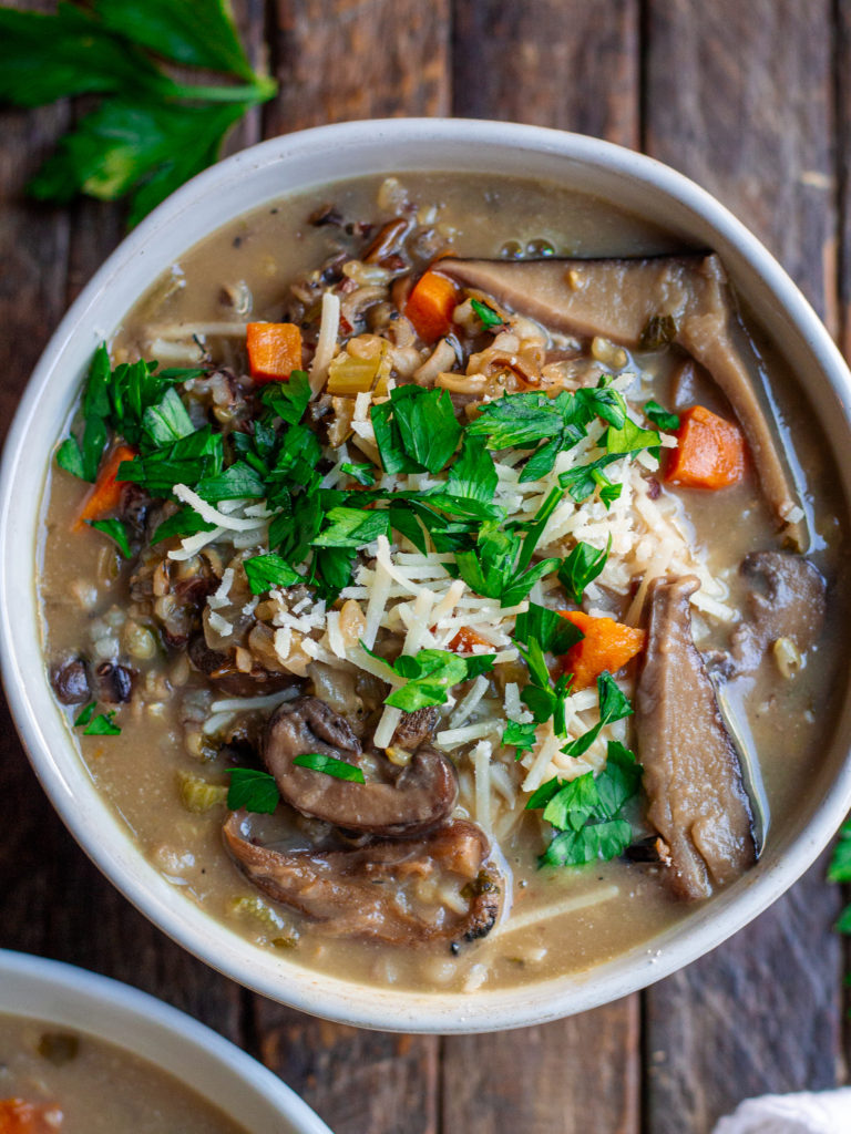 Bowl of creamy vegan wild rice and mushroom soup garnished with fresh parsley and vegan parmesan cheese.