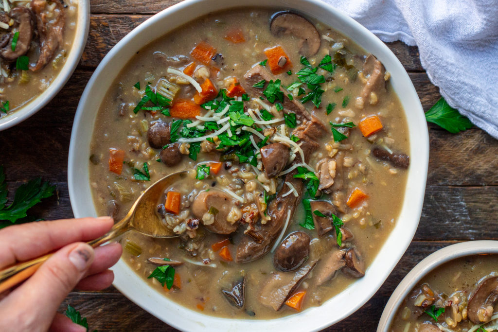 Bowl of creamy vegan wild rice and mushroom soup garnished with fresh parsley and vegan parmesan cheese.