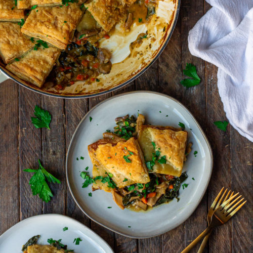 Golden-brown vegan mushroom pot pie with a flaky puff pastry crust, topped with fresh parsley.