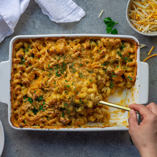 Golden-brown baked vegan mac and cheese in a casserole dish with a sprinkle of fresh parsley garnish.