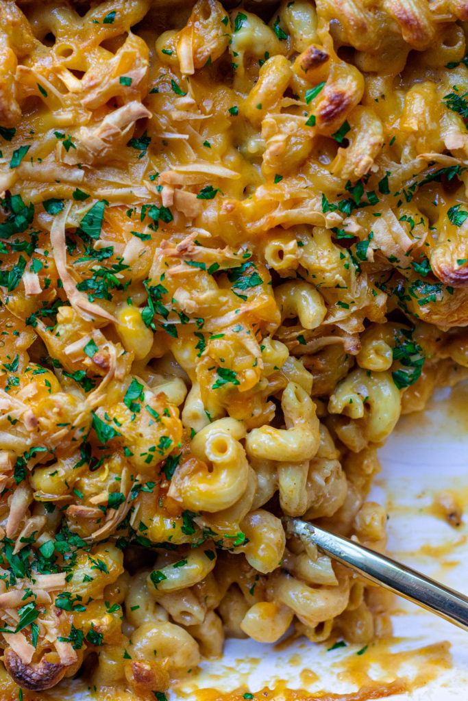 Golden-brown baked vegan mac and cheese in a casserole dish with a sprinkle of fresh parsley garnish.