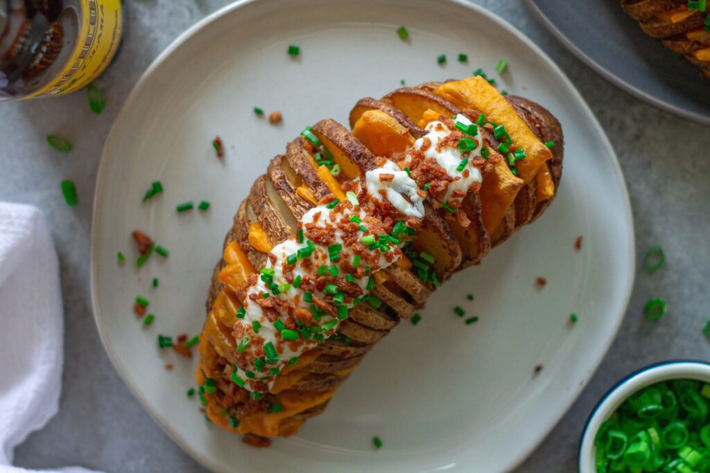 Close-up of a loaded Hasselback potato showing crispy edges, melted cheese, and fresh toppings.
