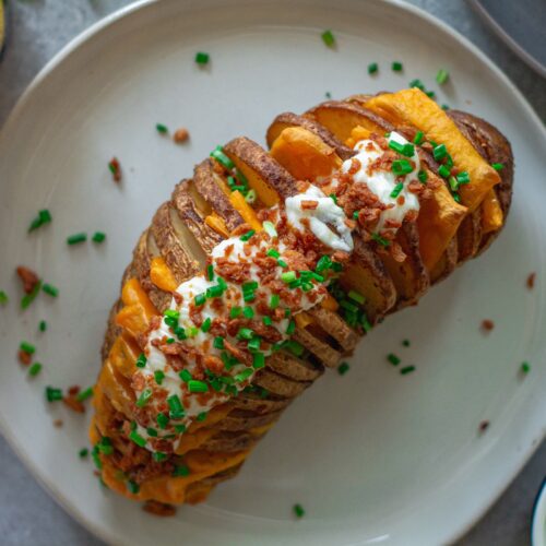 Close-up of a loaded Hasselback potato showing crispy edges, melted cheese, and fresh toppings.