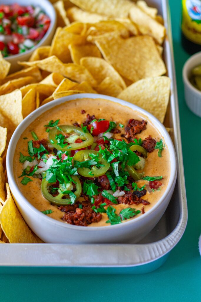 Close-up of creamy vegan queso dip with garnishes, showing the rich texture and colors.