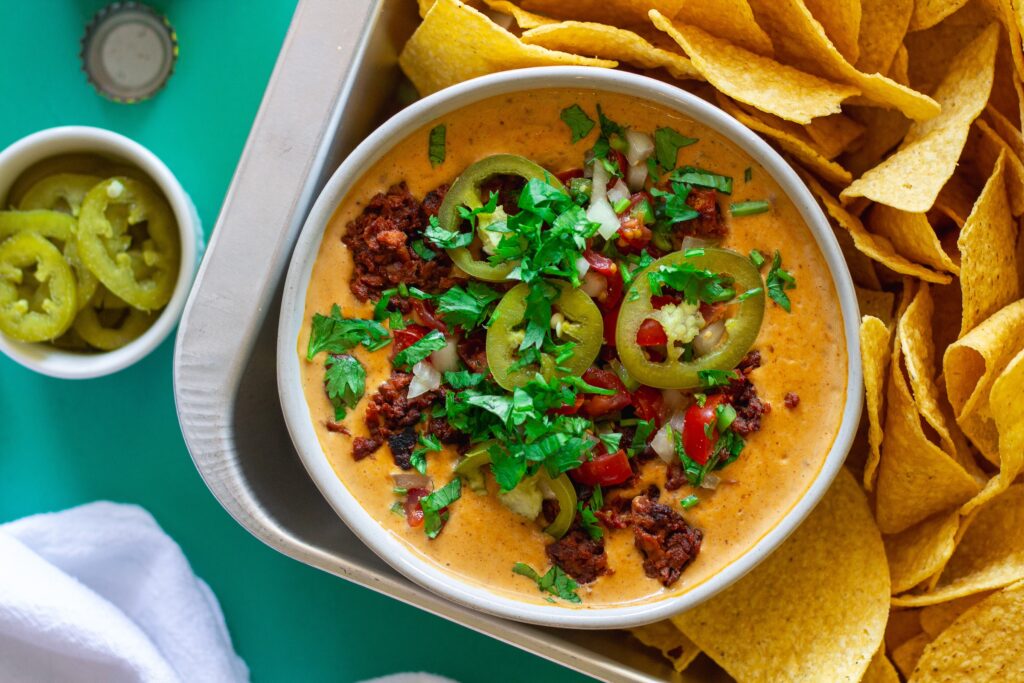 Close-up of creamy vegan queso dip with garnishes, showing the rich texture and colors.