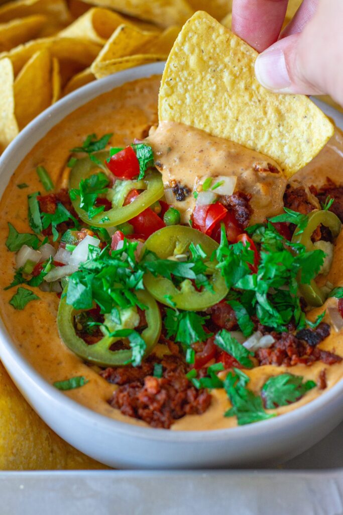 Close-up of creamy vegan queso dip with garnishes, showing the rich texture and colors.