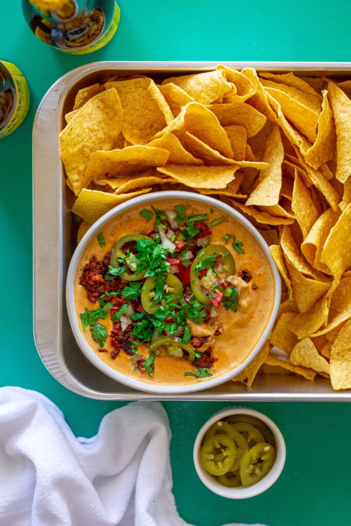 Close-up of creamy vegan queso dip with garnishes, showing the rich texture and colors.