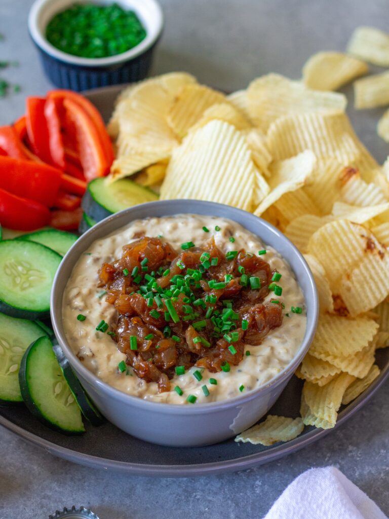 Vegan caramelized onion dip served with chips and fresh vegetables on a platter.