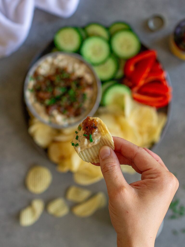 Close-up shot of creamy vegan caramelized onion dip with a chip being dipped.