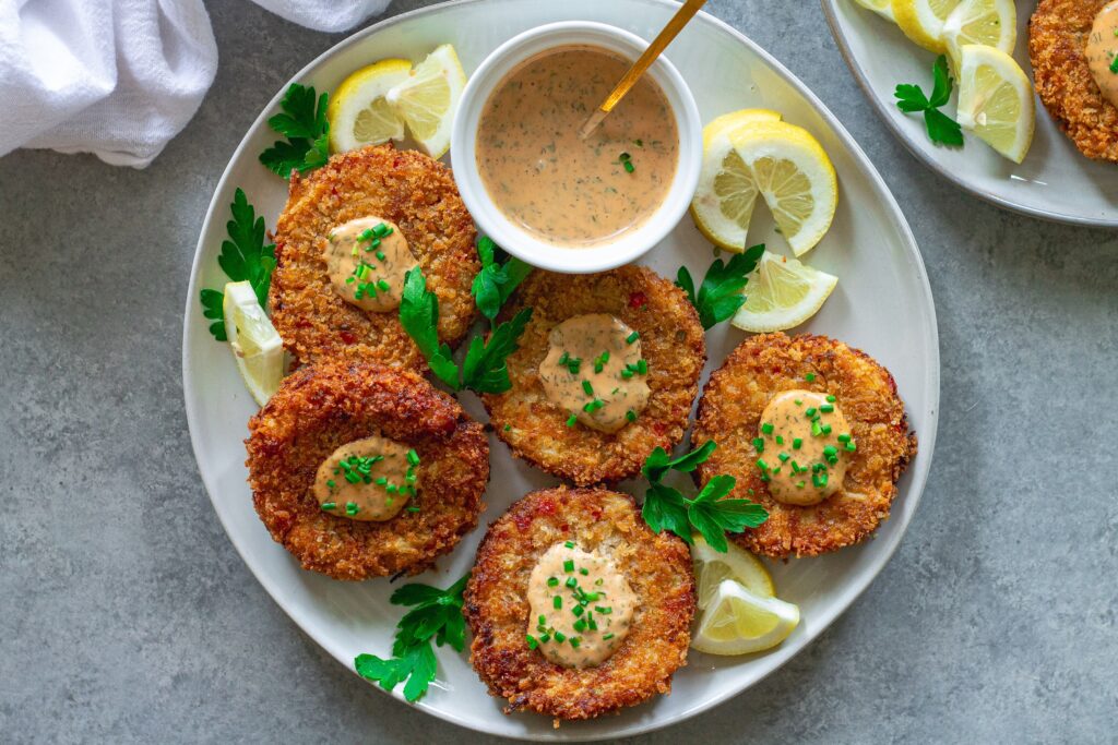 Vegan crab cakes served on a platter with a side of dill remoulade and lemon wedges, ready to enjoy.