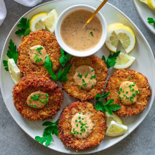 Vegan crab cakes served on a platter with a side of dill remoulade and lemon wedges, ready to enjoy.