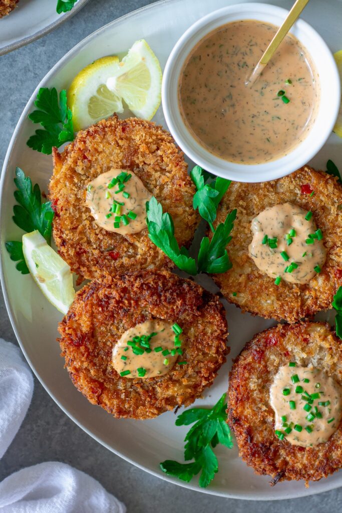 Crispy vegan crab cakes on a plate, garnished with fresh chives and served with dill remoulade.