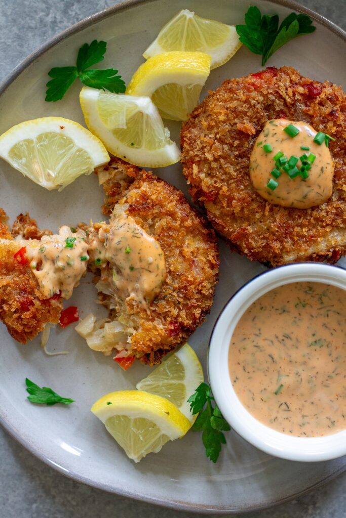 Crispy vegan crab cakes on a plate, garnished with fresh chives and served with dill remoulade.