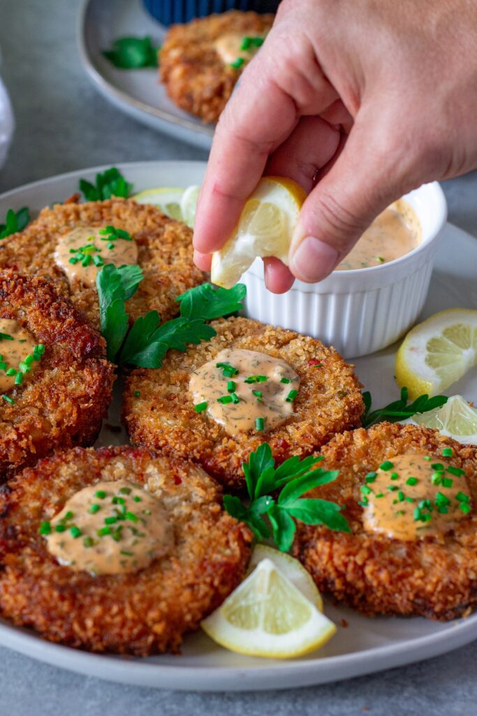 Crispy vegan crab cakes on a plate, garnished with fresh chives and served with dill remoulade.