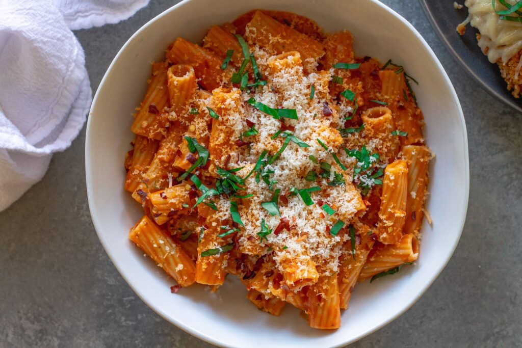 Creamy vegan spicy vodka pasta garnished with fresh basil and red pepper flakes, served in a white bowl.