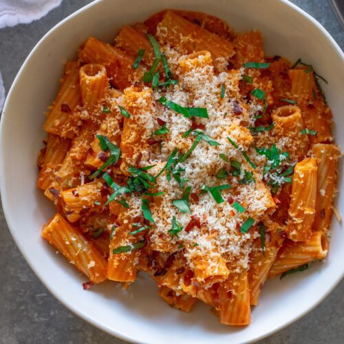 Creamy vegan spicy vodka pasta garnished with fresh basil and red pepper flakes, served in a white bowl.