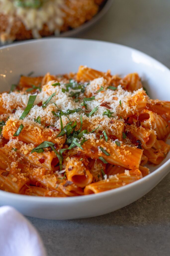 Creamy vegan spicy vodka pasta garnished with fresh basil and red pepper flakes, served in a white bowl.