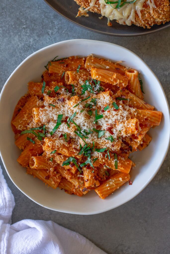 Creamy vegan spicy vodka pasta garnished with fresh basil and red pepper flakes, served in a white bowl.