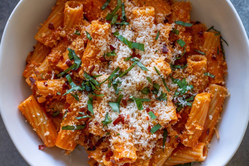 Creamy vegan spicy vodka pasta garnished with fresh basil and red pepper flakes, served in a white bowl.