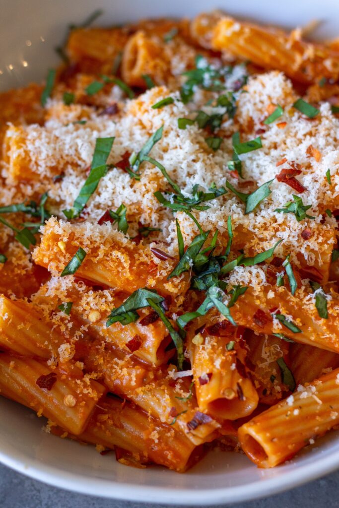 Creamy vegan spicy vodka pasta garnished with fresh basil and red pepper flakes, served in a white bowl.