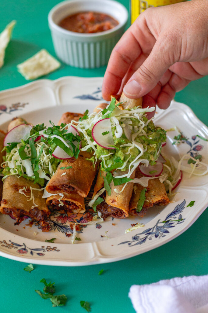 Crispy vegan black bean taquitos served with shredded cabbage and guacamole.