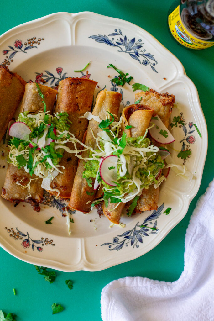 Crispy vegan black bean taquitos served with shredded cabbage and guacamole.