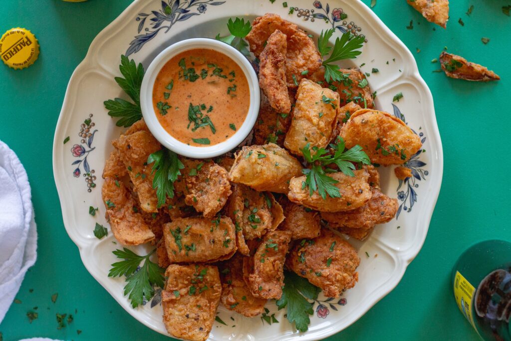 Crispy vegan bloomin' onion petals garnished with fresh parsley, served with a tangy dipping sauce on the side.