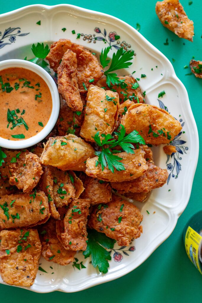 Crispy vegan bloomin' onion petals garnished with fresh parsley, served with a tangy dipping sauce on the side.