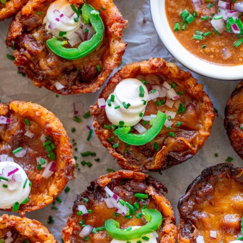 Platter of baked vegan chili cheese tater tot bites, garnished with sliced jalapeños, vegan sour cream, and red onion.