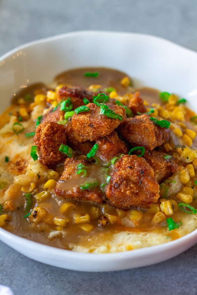 Vegan KFC Copycat Famous Bowl with mashed potatoes, roasted corn, crispy tofu, melted vegan cheese, and gravy in a bowl, garnished with green onions.