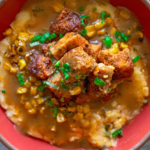 Vegan KFC Copycat Famous Bowl with mashed potatoes, roasted corn, crispy tofu, melted vegan cheese, and gravy in a bowl, garnished with green onions.