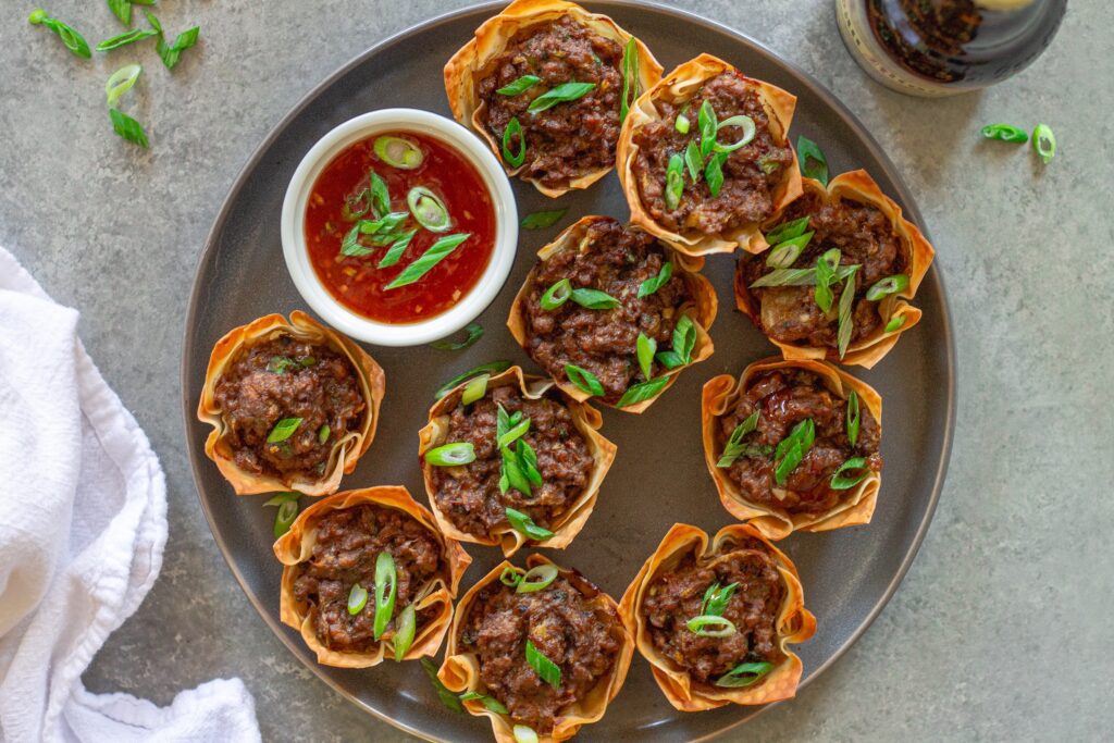 Platter of Vegan Lumpia Wonton Cups, ready to serve, with a side of sweet chili dipping sauce and fresh chive garnish.