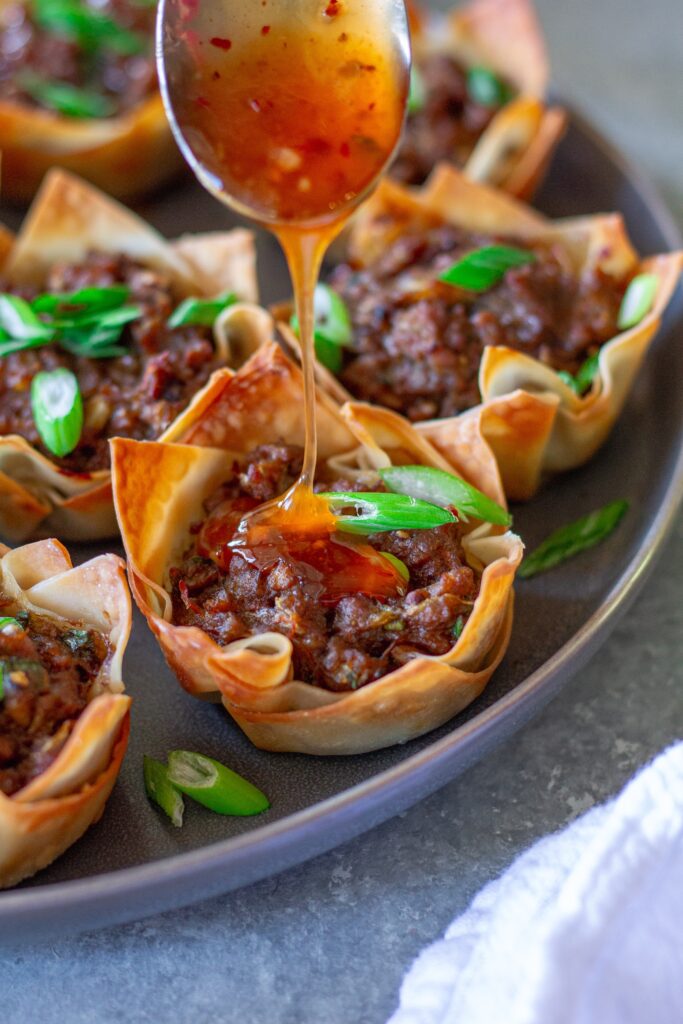 Vegan Lumpia Wonton Cup being dipped into sweet chili sauce, highlighting its crispy edges and flavorful filling.