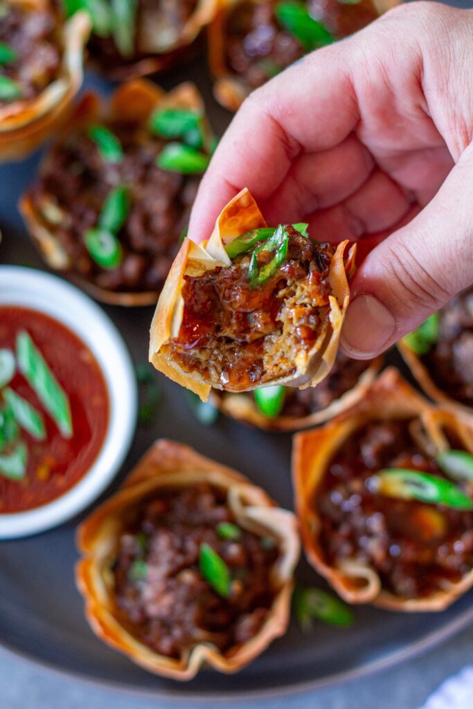 Vegan Lumpia Wonton Cup with a bite taken out, revealing the seasoned vegan ground beef and vegetable filling inside.