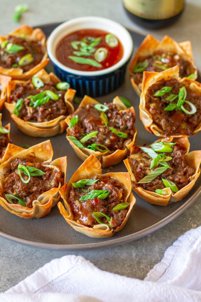 Platter of Vegan Lumpia Wonton Cups, ready to serve, with a side of sweet chili dipping sauce and fresh chive garnish.