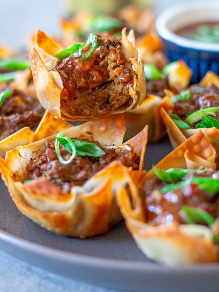 Vegan Lumpia Wonton Cup with a bite taken out, revealing the seasoned vegan ground beef and vegetable filling inside.