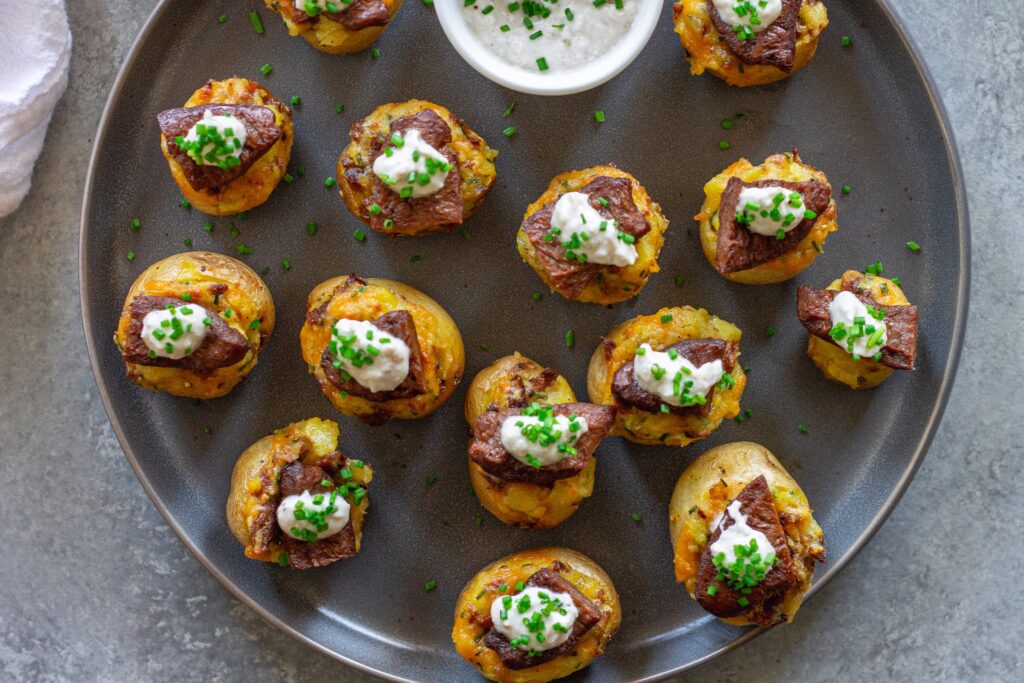 Plate of vegan steak ‘n’ potato bites served with a small bowl of garlic horseradish dipping sauce, garnished with fresh chives.